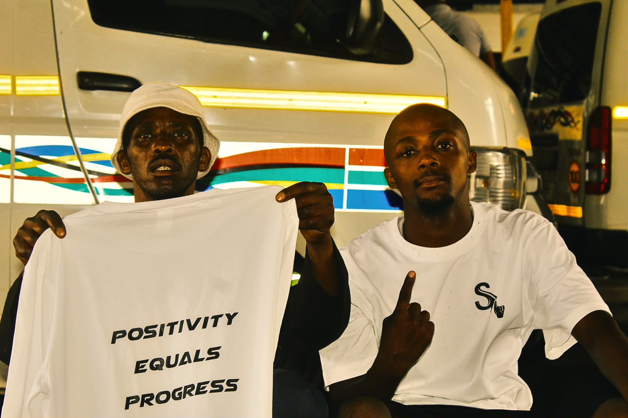Positivity Equals Progress tee held up by the Sqedi Mandatory community